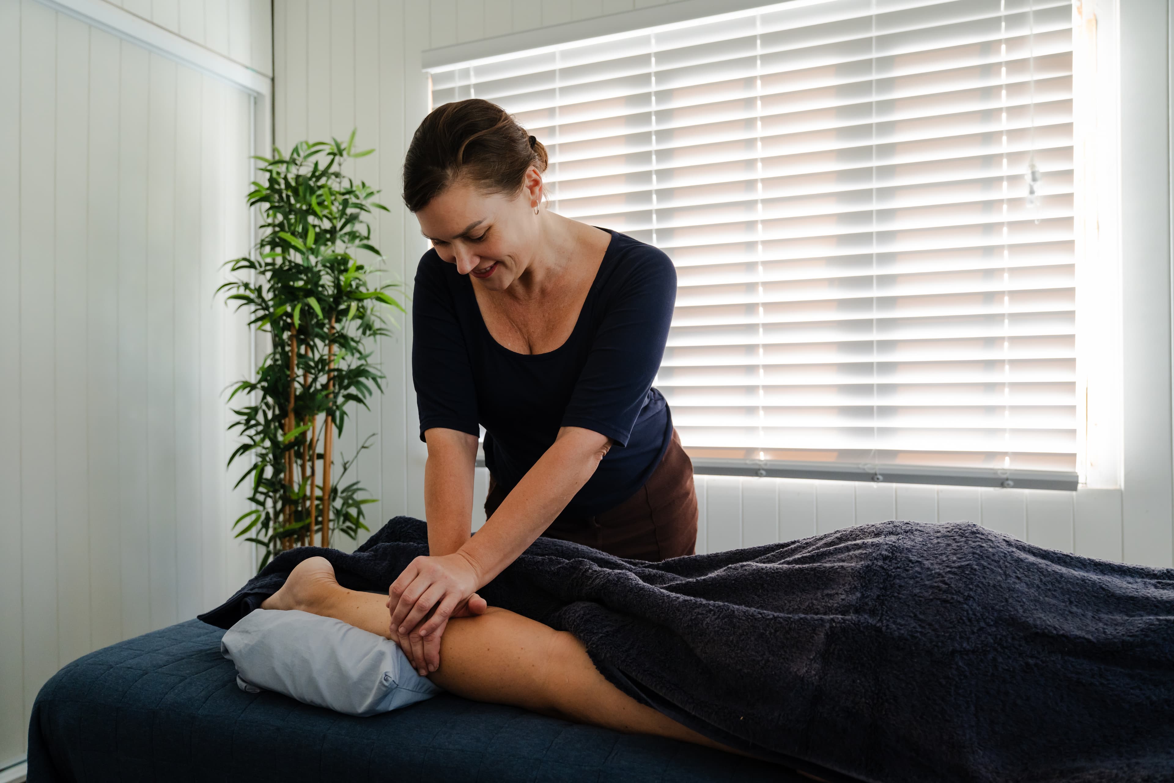 Sid applying deep tissue pressure to the calf, hamstring and knee region of a client on the treatment table, targeting leg pain and knee restriction at Seabreeze Bodywork.